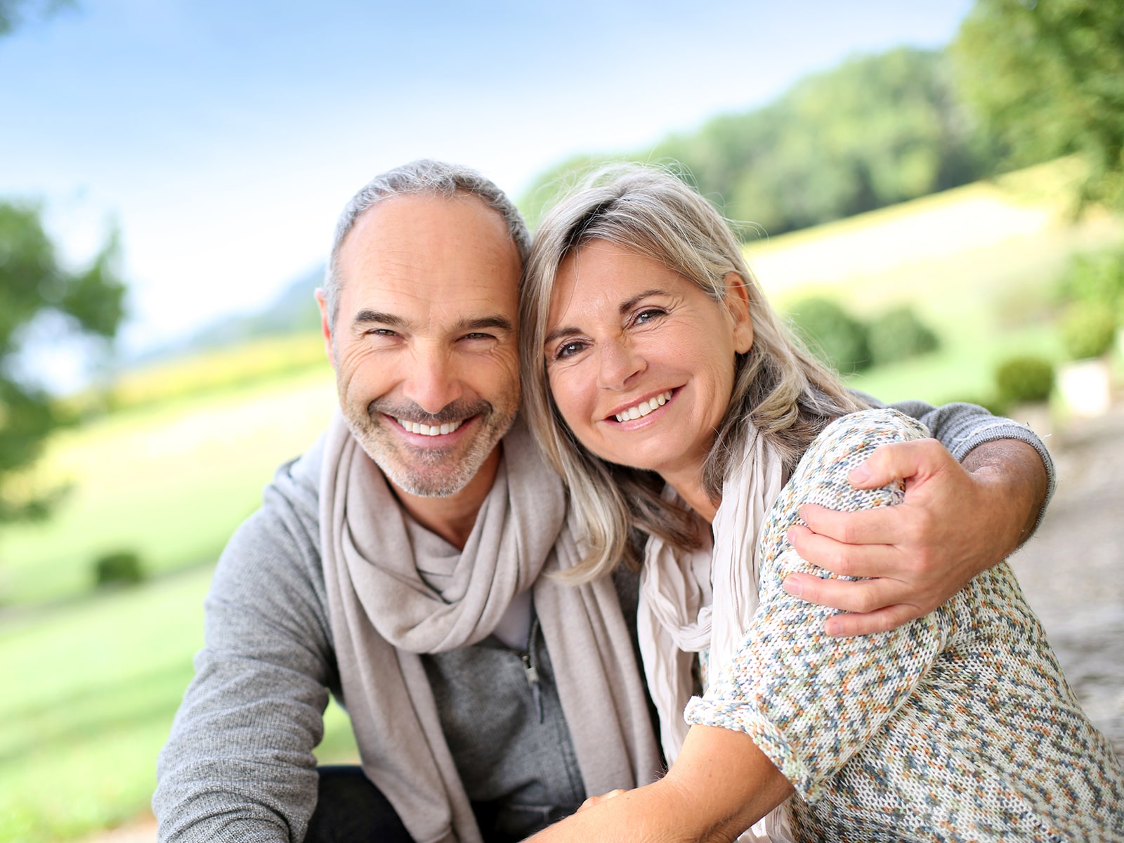 Middle-aged couple sitting outdoors, sharing a side hug.