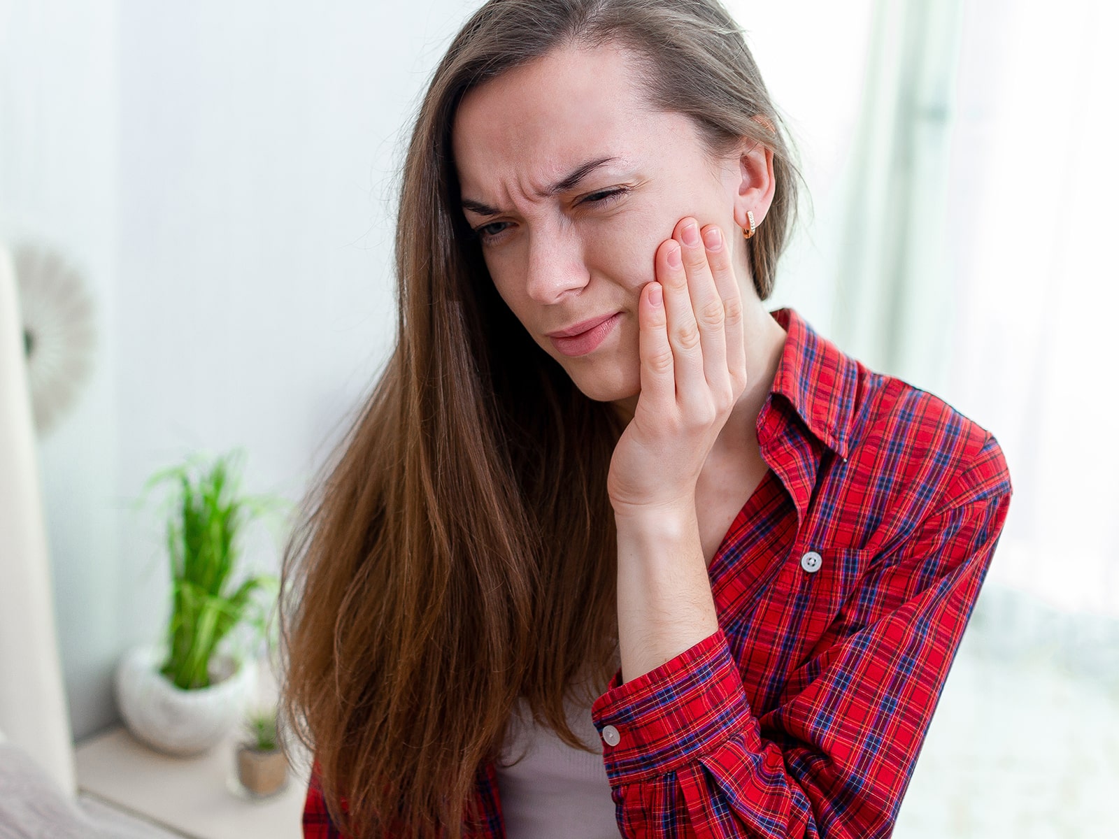 Young man with brown hair wearing a red plaid shirt, experiencing jaw pain.