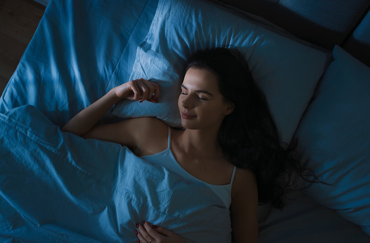 Beautiful young woman resting on blue sheets with moonlight streaming through the window.