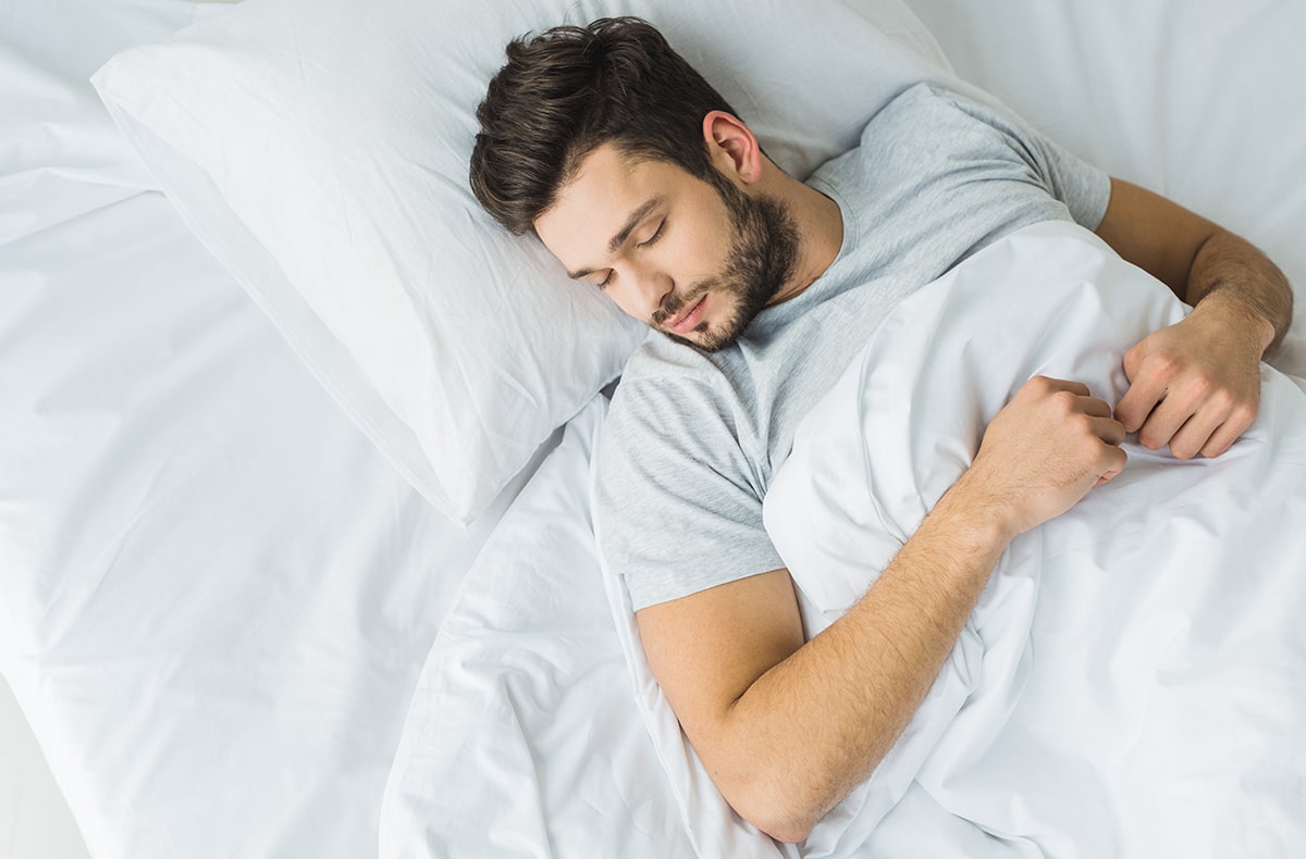 Man enjoying quality sleep in bed with white sheets.
