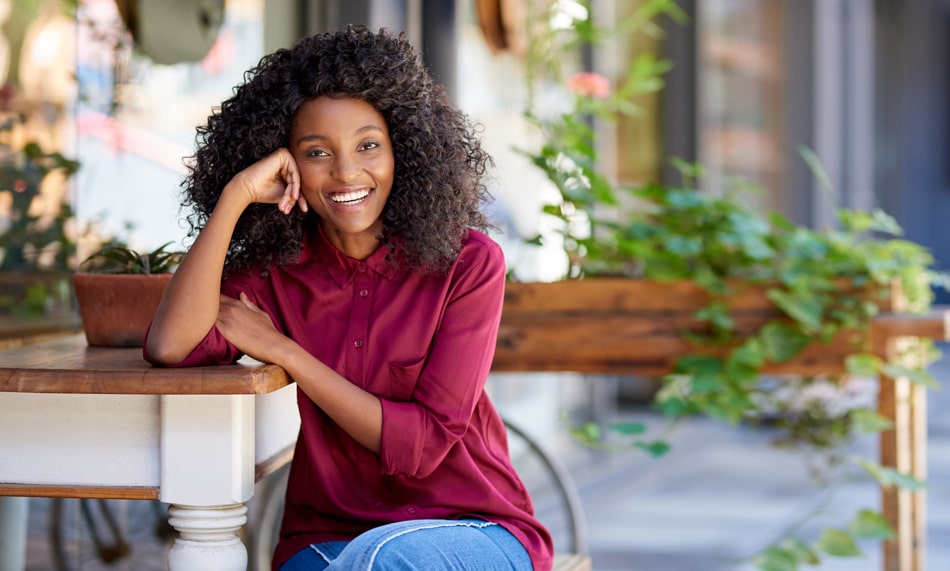 Woman sitting at a table, showing off her new smile with Porcelain Veneers