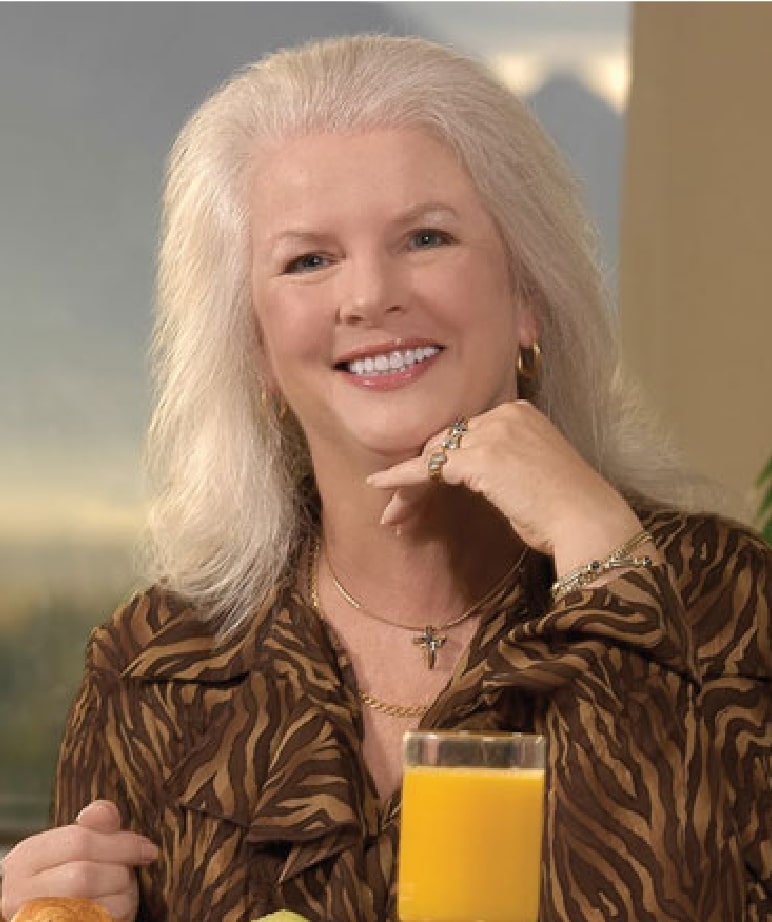 Woman smiling near a glass of orange juice, wearing a leopard print shirt.