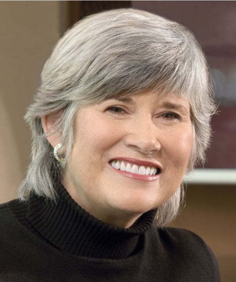 Woman with gray hair wearing a turtleneck, displaying a big smile thanks to dental implants from her dentist