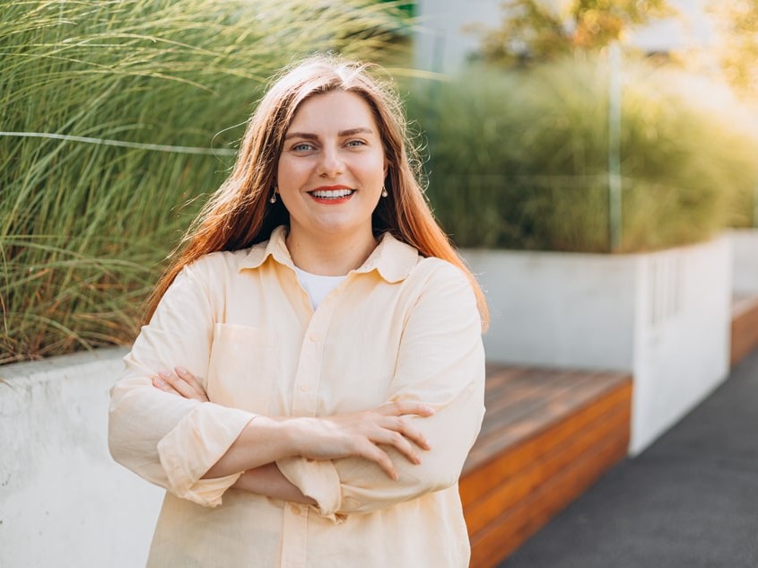 woman standing outside arm folded smiling with teeth